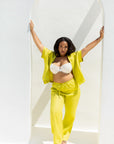 A woman posing in a bright yellow two-piece lounge set consisting of a short-sleeve top and matching drawstring pants, styled with a white bralette and white sneakers, set against a white arched wall.