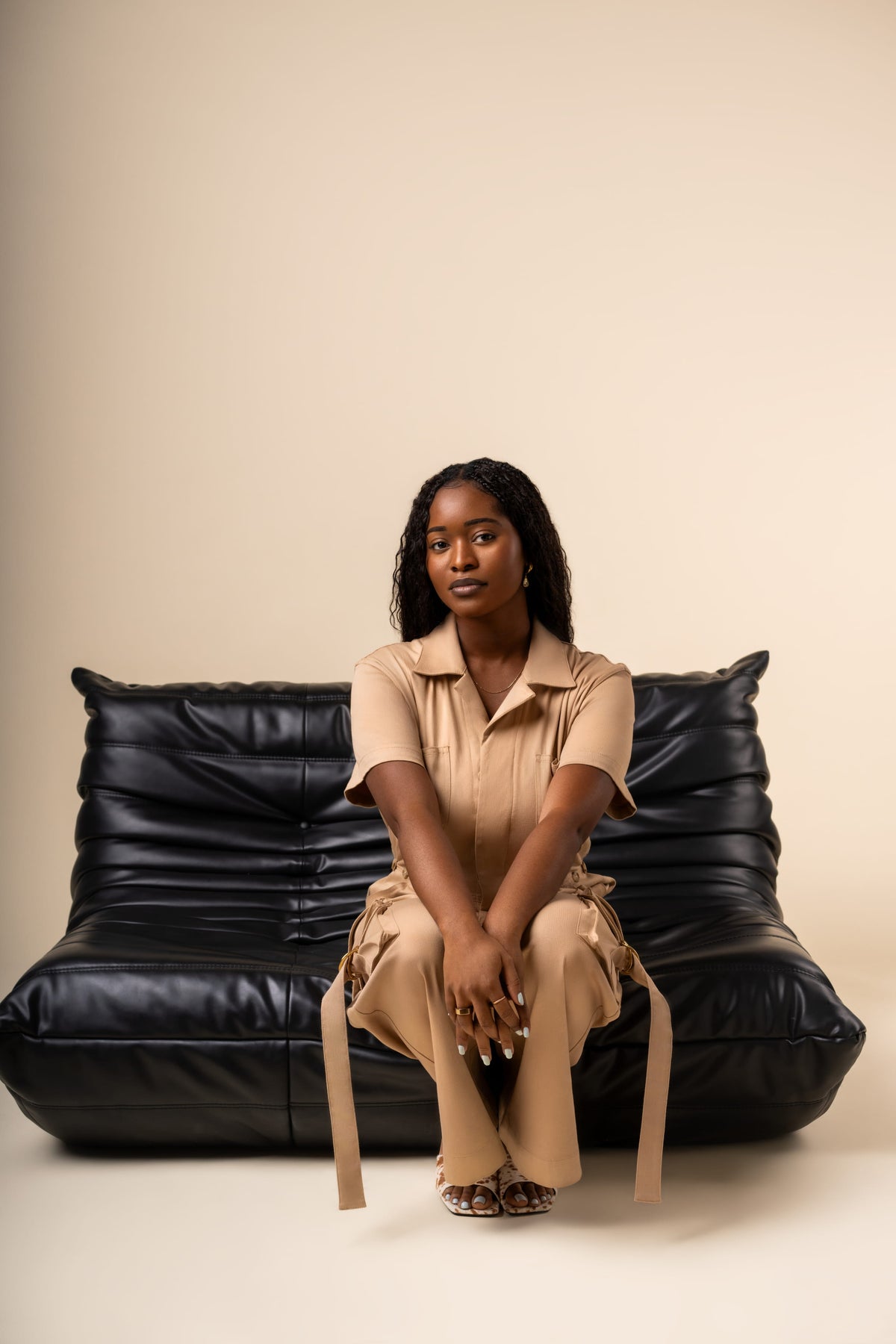 Woman sitting on a black leather couch against a beige background