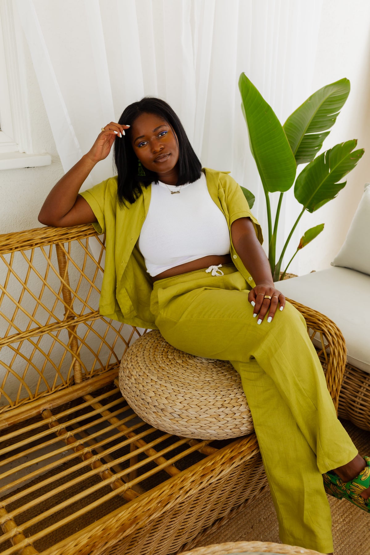 Woman in a green outfit sitting on a wicker chair with a plant in the background